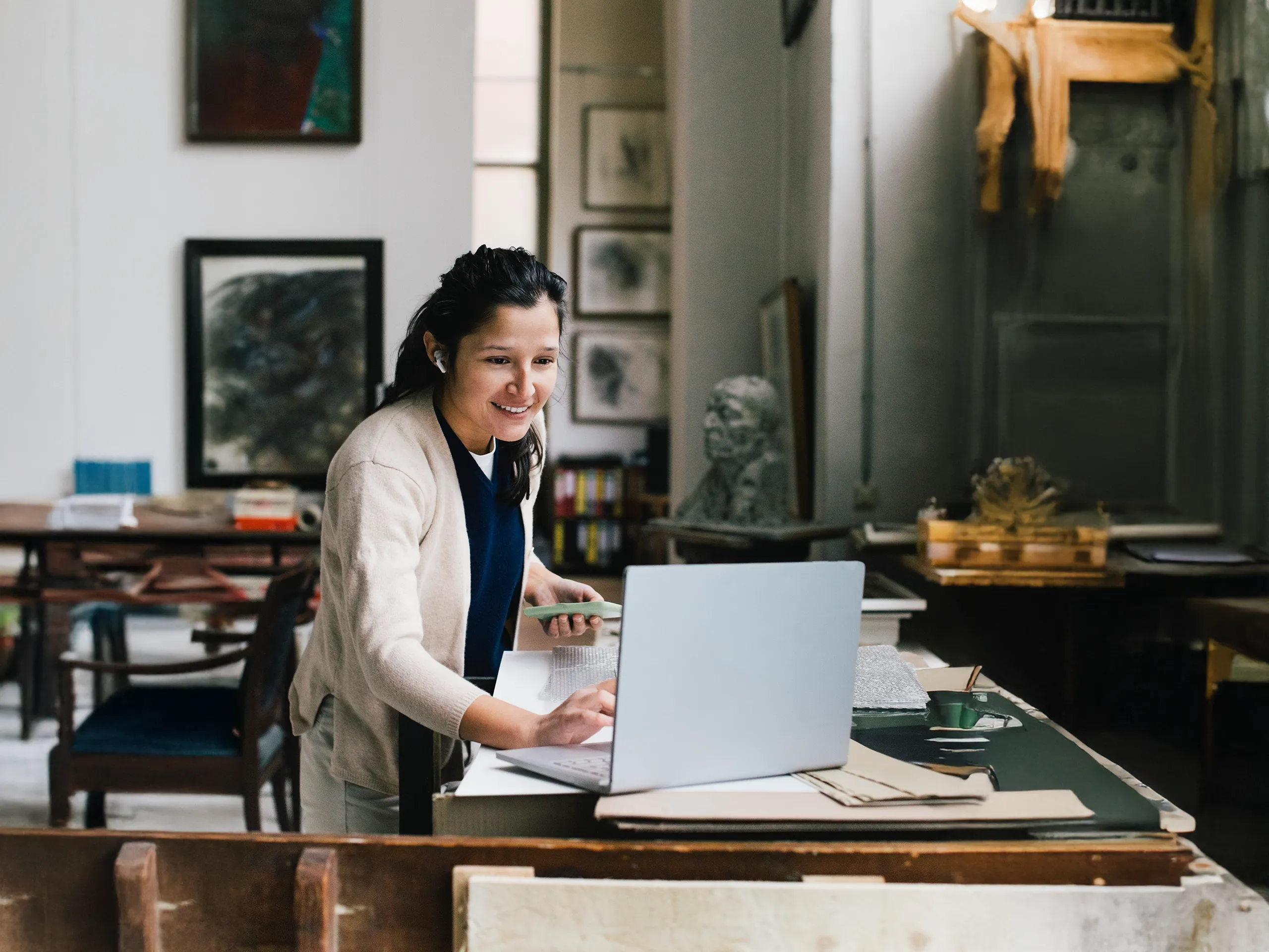 Lächelnde Frau arbeitet mit Laptop in einem kreativen Atelier.